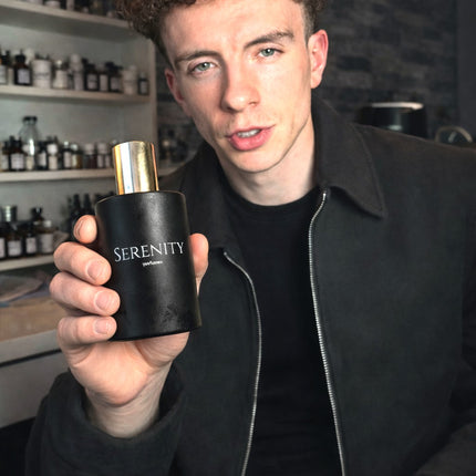 Person holding a black 'Serenity' perfume bottle in a store setting